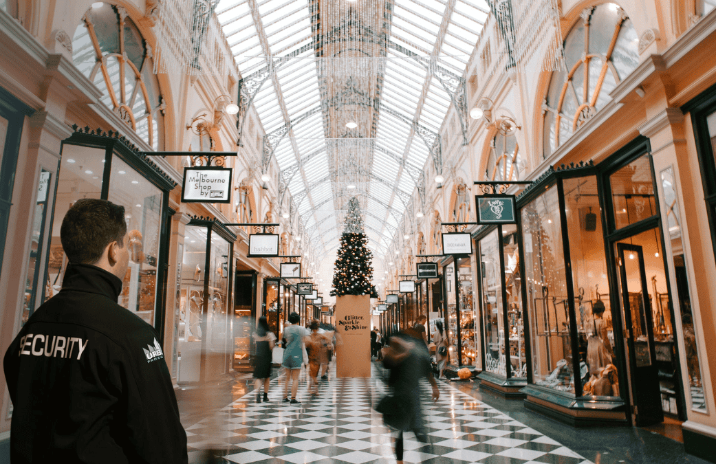 Urban Protection Group security guard monitors a busy holiday shopping mall with Christmas decoration, ensuring safety and order.